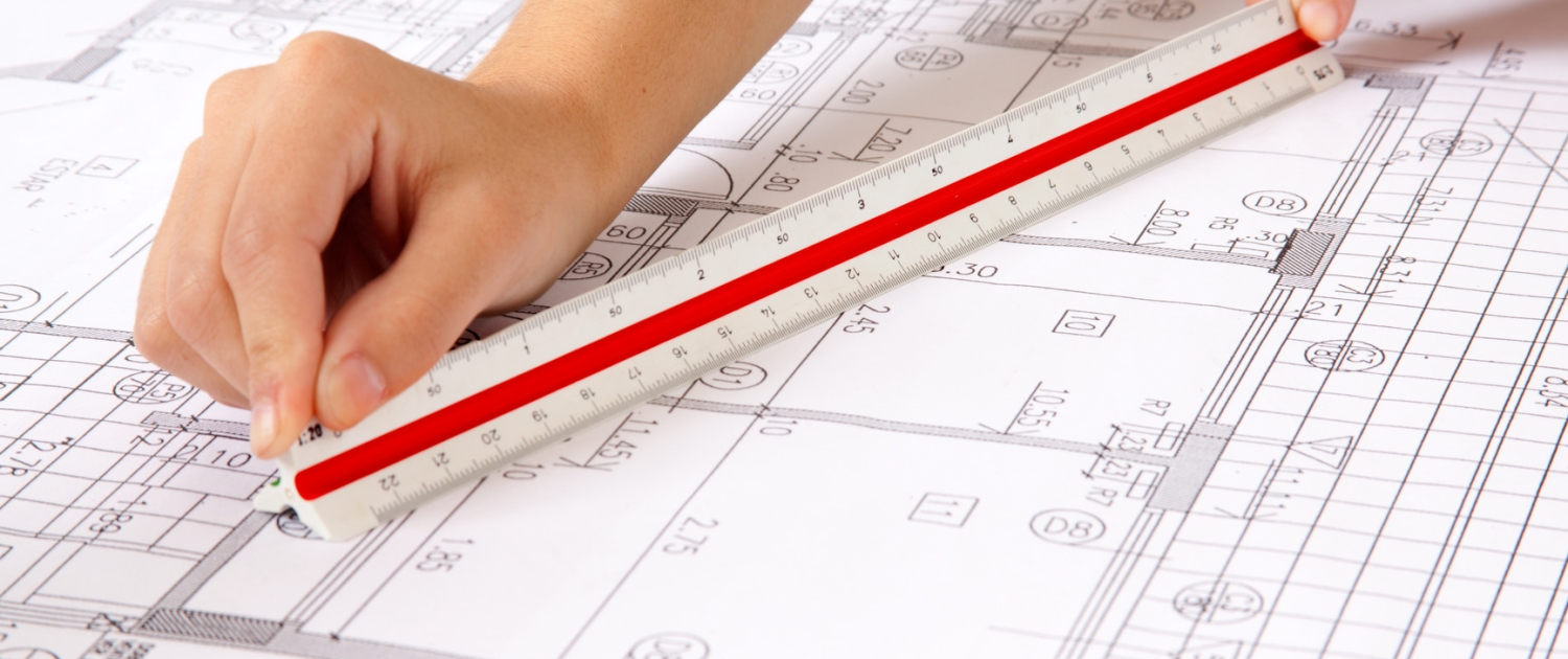 Two hands using a scale ruler on a set of blueprints
